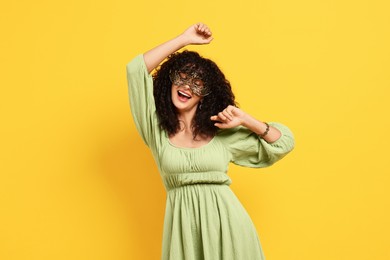 Happy young woman wearing carnival mask on yellow background