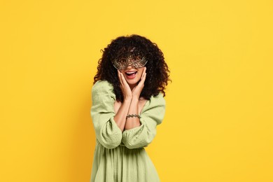 Photo of Happy young woman wearing carnival mask on yellow background