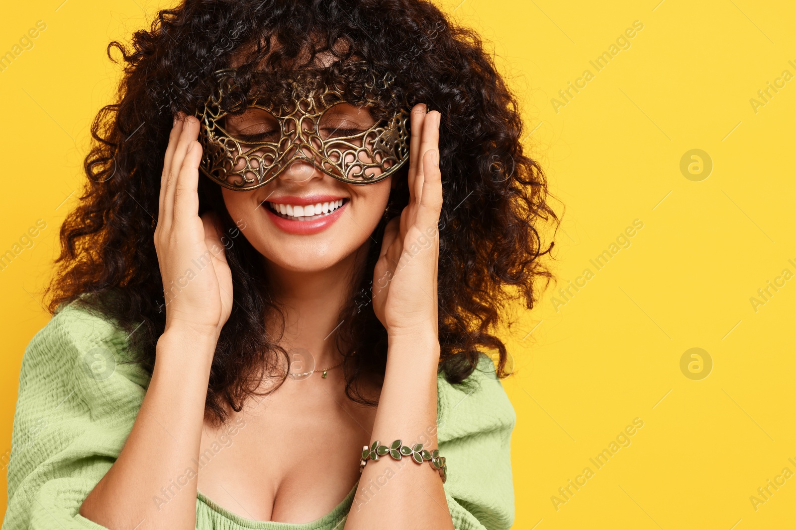 Photo of Happy young woman wearing carnival mask on yellow background