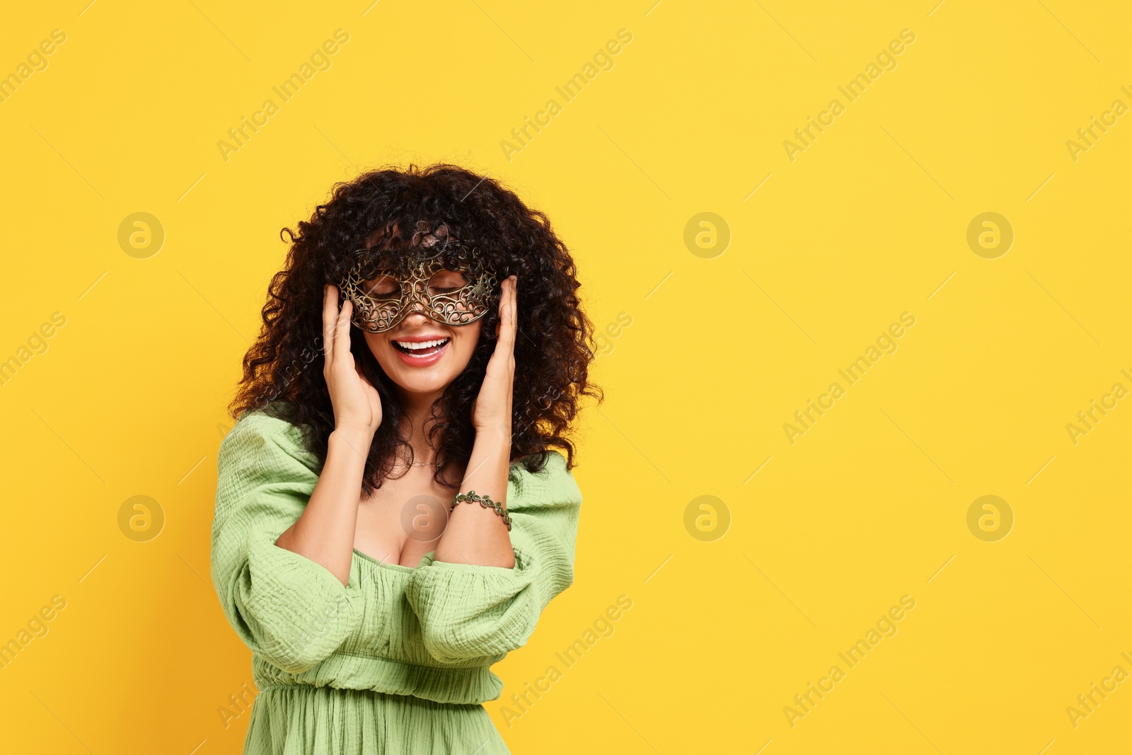 Photo of Happy young woman wearing carnival mask on yellow background, space for text