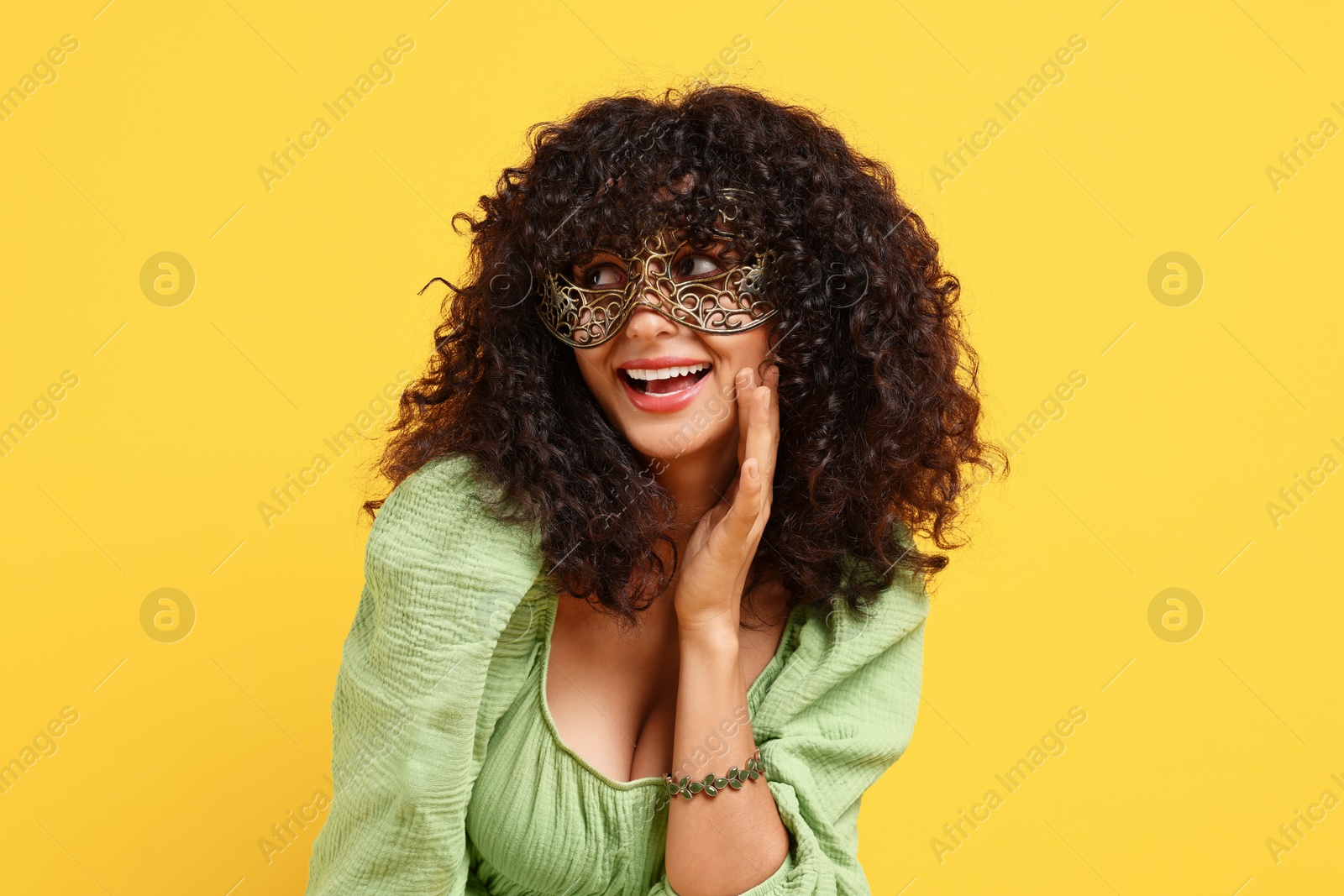 Photo of Happy young woman wearing carnival mask on yellow background