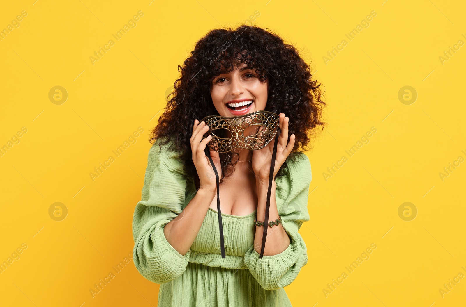 Photo of Smiling young woman with carnival mask on yellow background