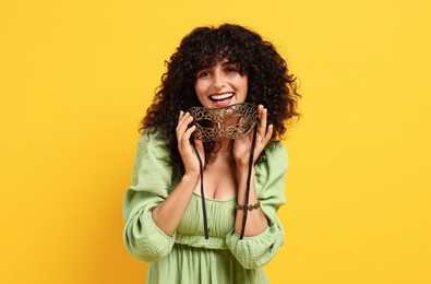 Smiling young woman with carnival mask on yellow background