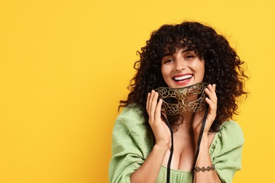 Photo of Smiling young woman with carnival mask on yellow background, space for text