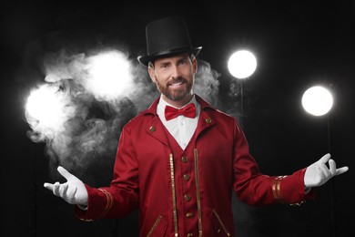 Portrait of showman in red costume and hat on black background with spotlights and smoke