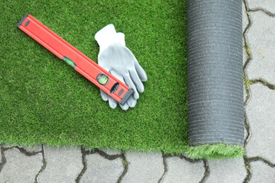 Photo of Gloves, level tool and roll of artificial turf outdoors, top view