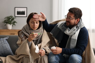 Photo of Cold symptom. Couple suffering from fever on sofa at home