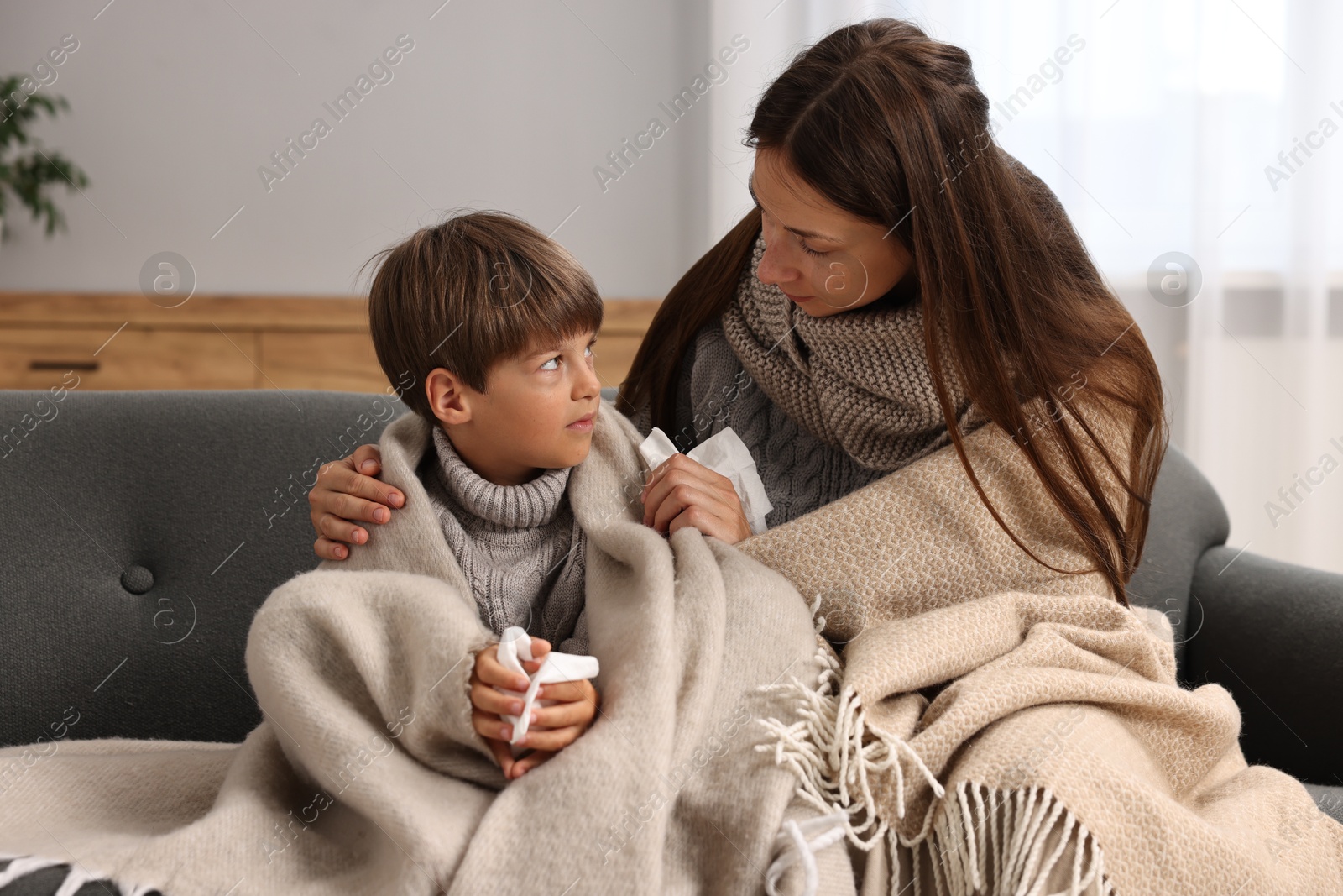 Photo of Cold symptom. Woman with her son suffering from fever on sofa at home