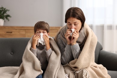 Photo of Cold symptom. Woman with her son suffering from fever on sofa at home