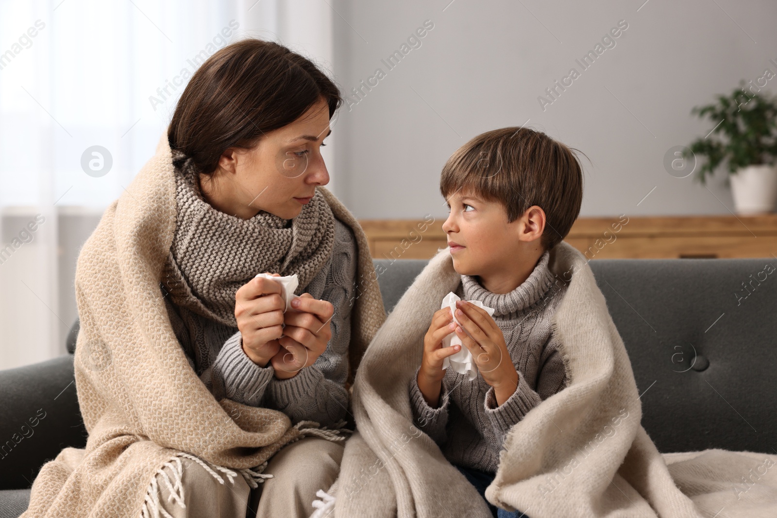 Photo of Cold symptom. Woman with her son suffering from fever on sofa at home