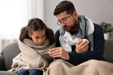 Cold symptom. Father with his daughter suffering from fever on sofa at home