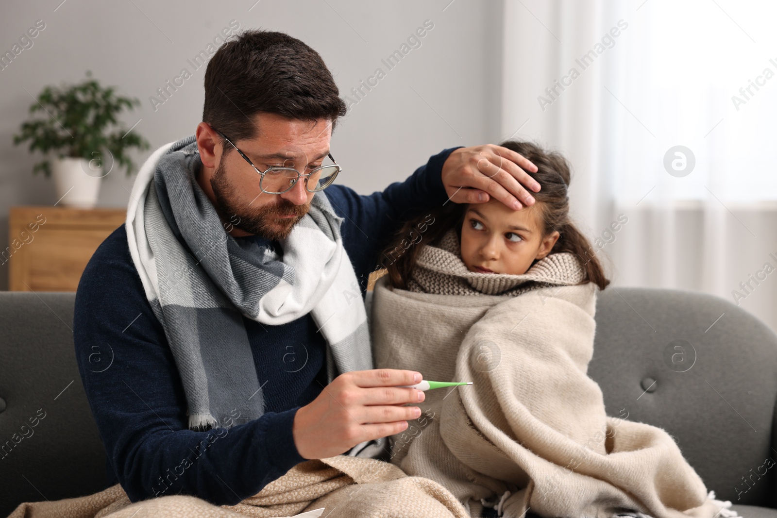 Photo of Cold symptom. Father with his daughter suffering from fever on sofa at home