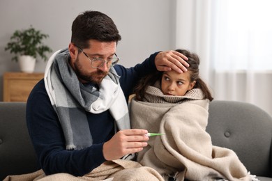 Cold symptom. Father with his daughter suffering from fever on sofa at home