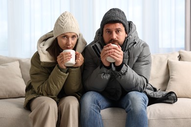 Cold symptom. Couple with cups of drink suffering from fever on sofa at home