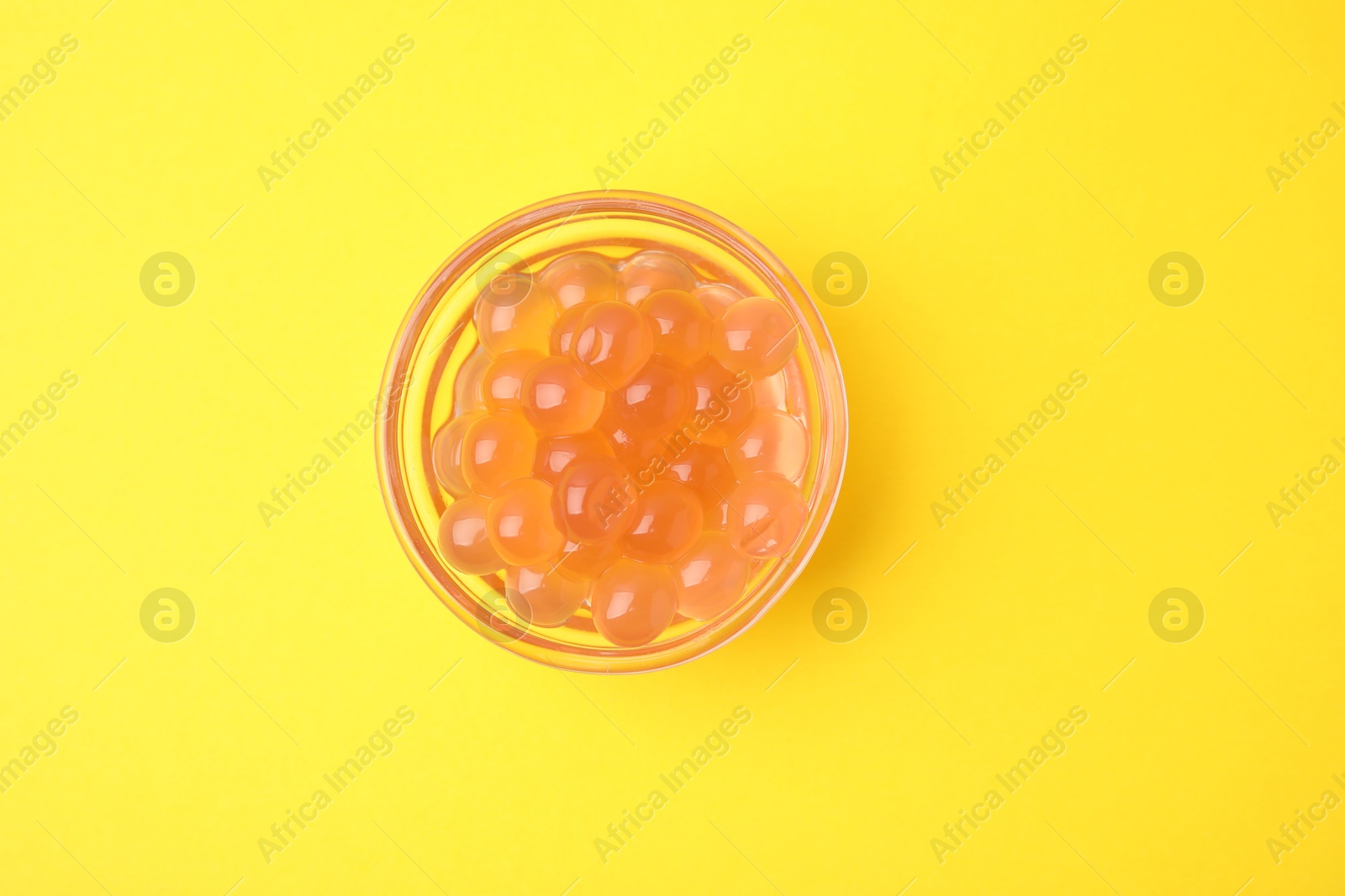 Photo of Bright tapioca pearls in bowl on yellow background, top view