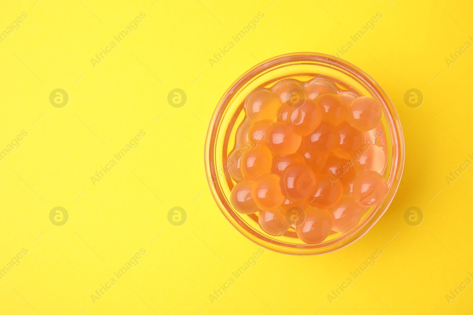 Photo of Bright tapioca pearls in bowl on yellow background, top view. Space for text