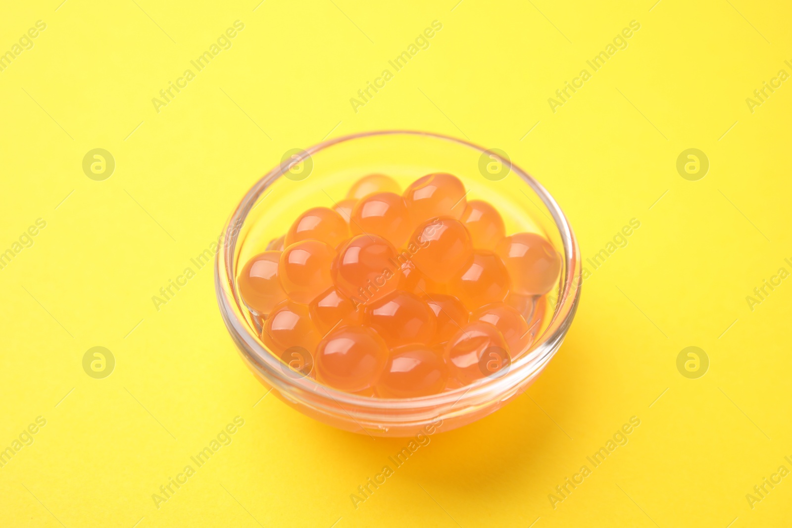 Photo of Bright tapioca pearls in bowl on yellow background, closeup