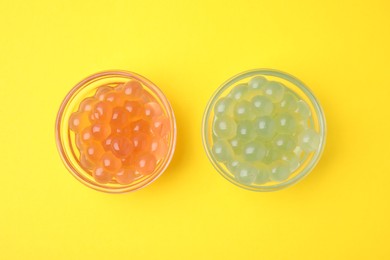 Photo of Bright tapioca pearls in bowls on yellow background, flat lay