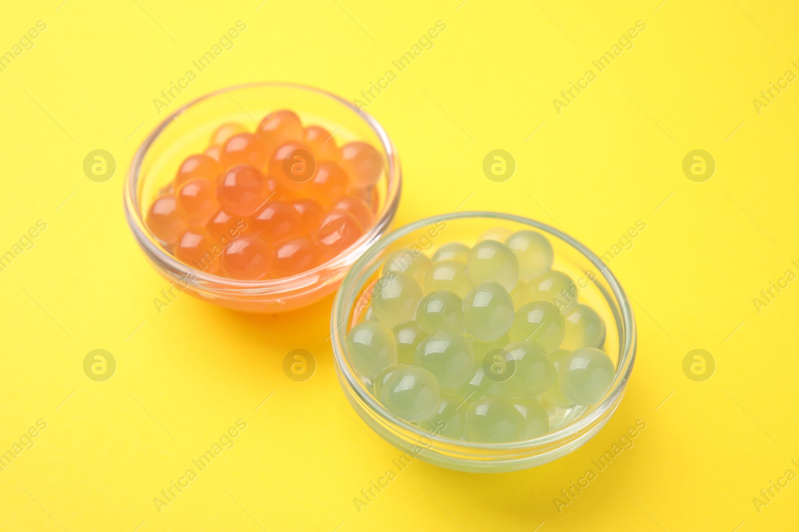 Photo of Bright tapioca pearls in bowls on yellow background, closeup