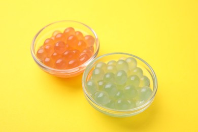 Photo of Bright tapioca pearls in bowls on yellow background, closeup