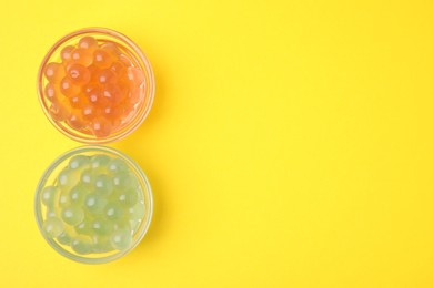 Photo of Bright tapioca pearls in bowls on yellow background, flat lay. Space for text