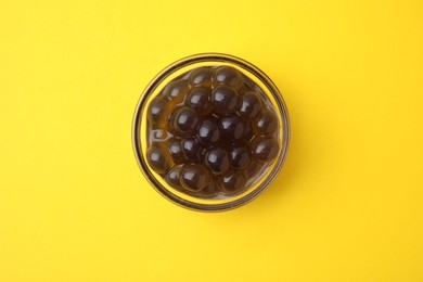 Photo of Dark tapioca pearls in bowl on yellow background, top view