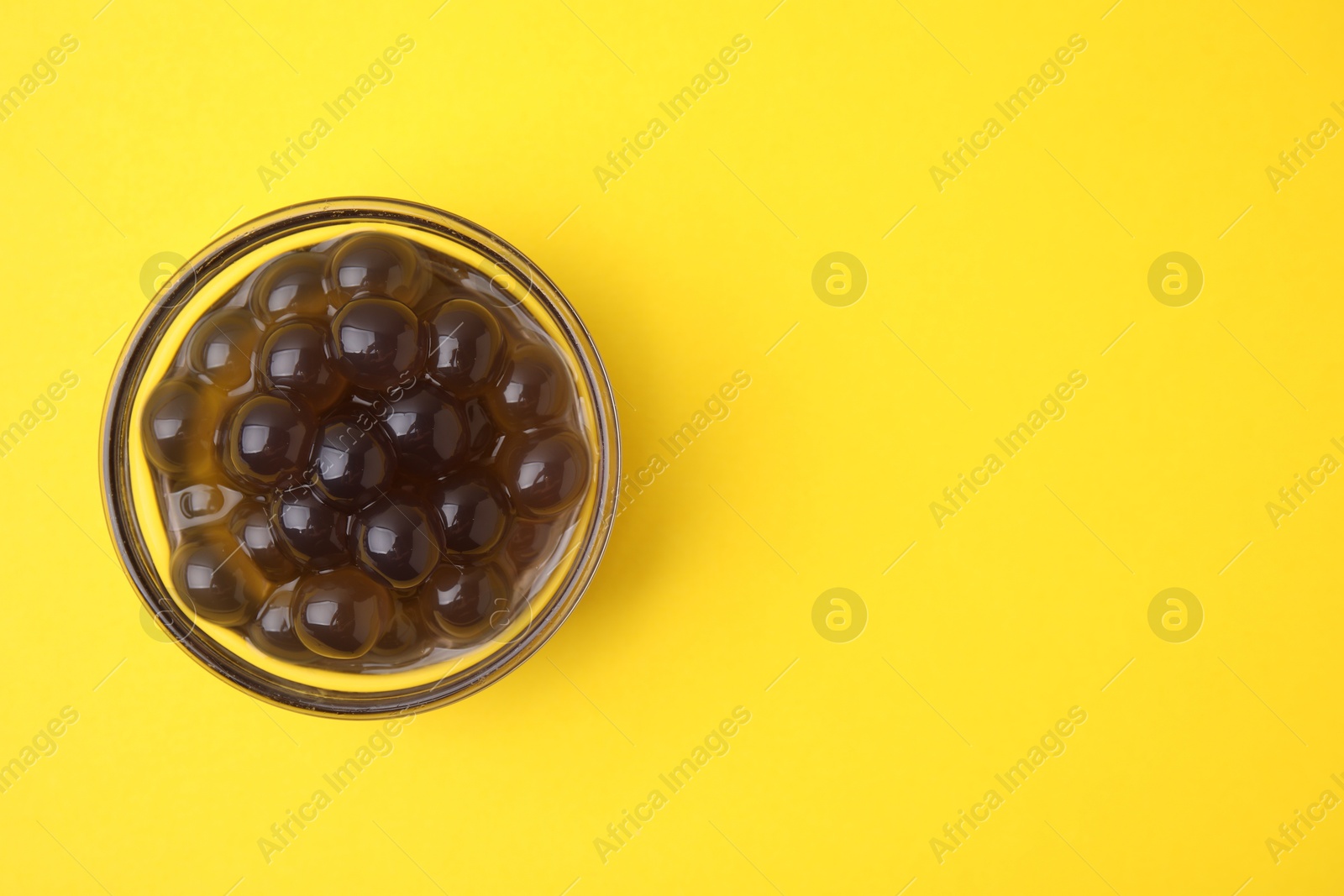 Photo of Dark tapioca pearls in bowl on yellow background, top view. Space for text