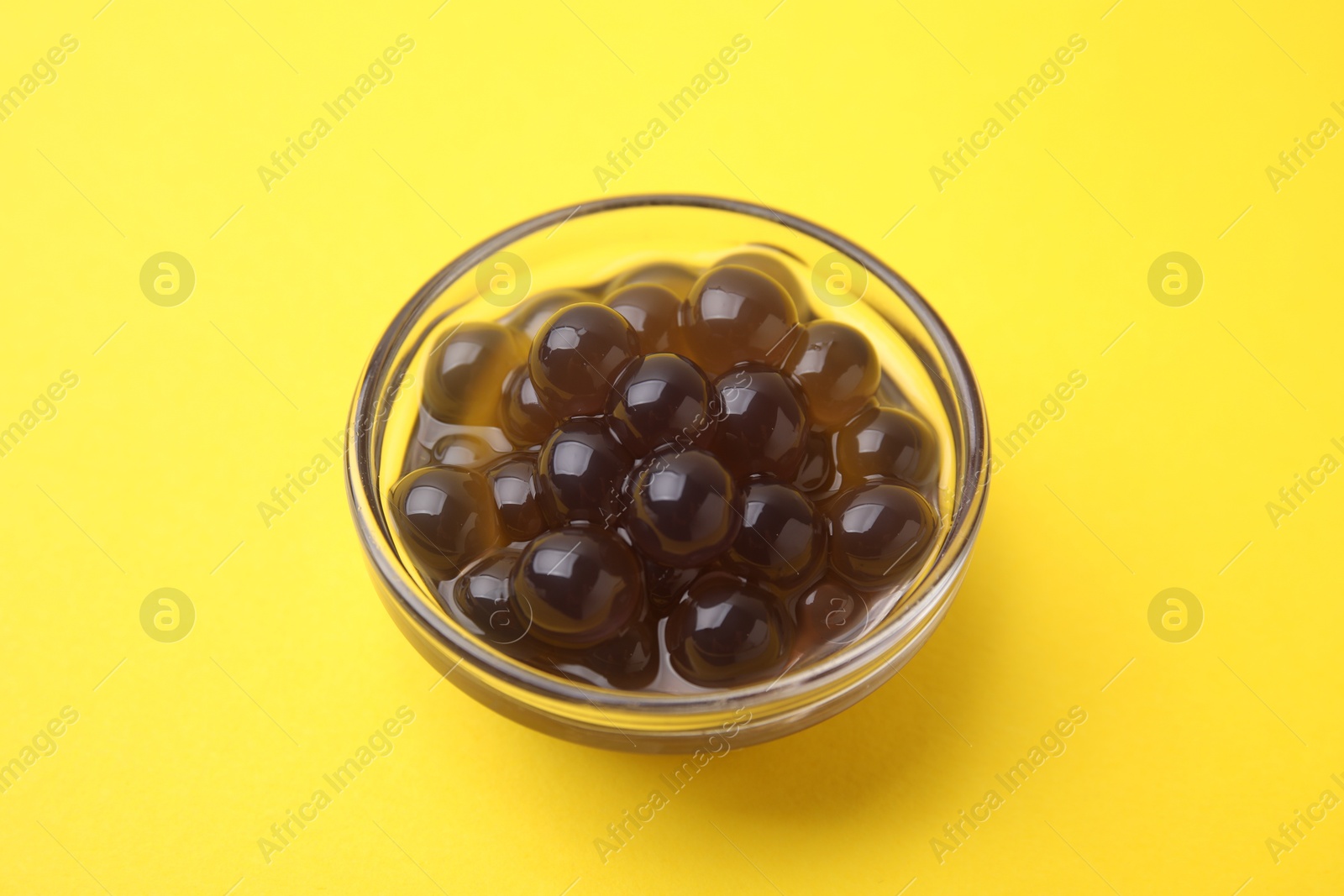 Photo of Dark tapioca pearls in bowl on yellow background, closeup