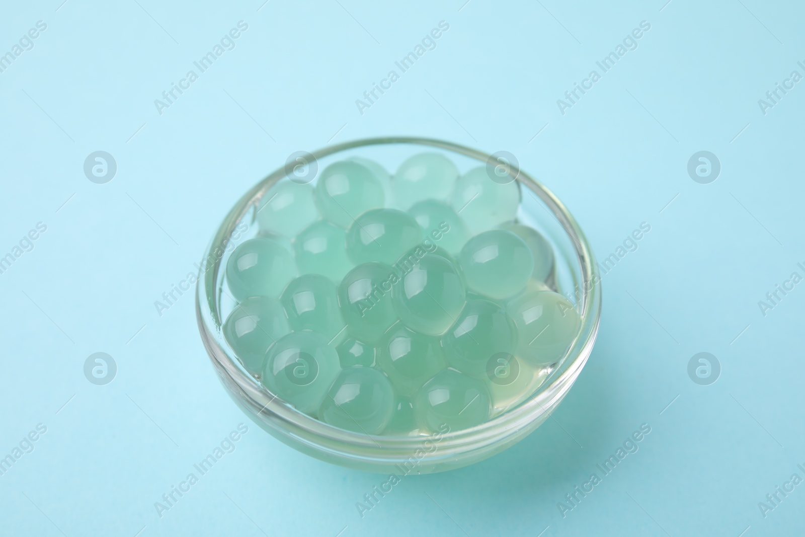 Photo of Bright tapioca pearls in bowl on light blue background, closeup