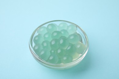 Bright tapioca pearls in bowl on light blue background, closeup