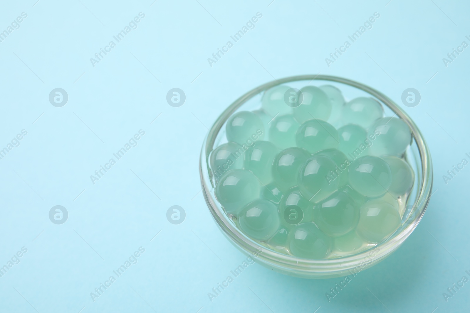 Photo of Bright tapioca pearls in bowl on light blue background, closeup. Space for text