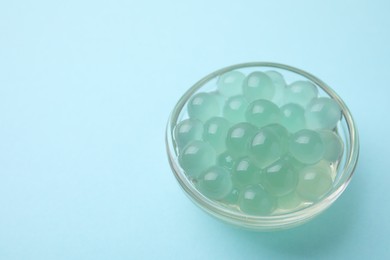 Photo of Bright tapioca pearls in bowl on light blue background, closeup. Space for text