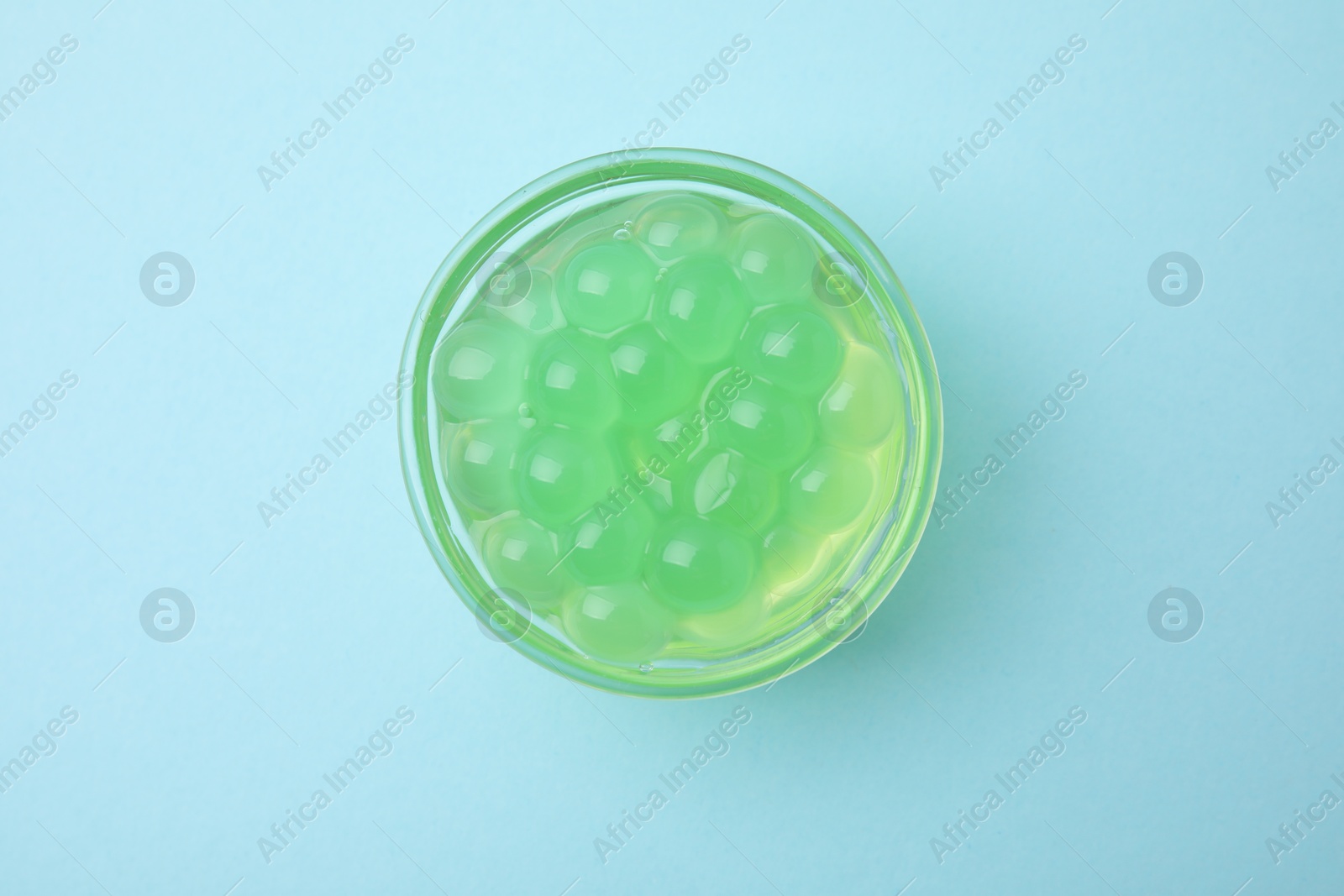 Photo of Bright tapioca pearls in bowl on light blue background, top view