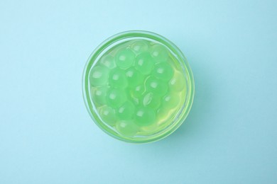 Bright tapioca pearls in bowl on light blue background, top view