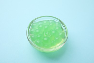 Photo of Bright tapioca pearls in bowl on light blue background, closeup