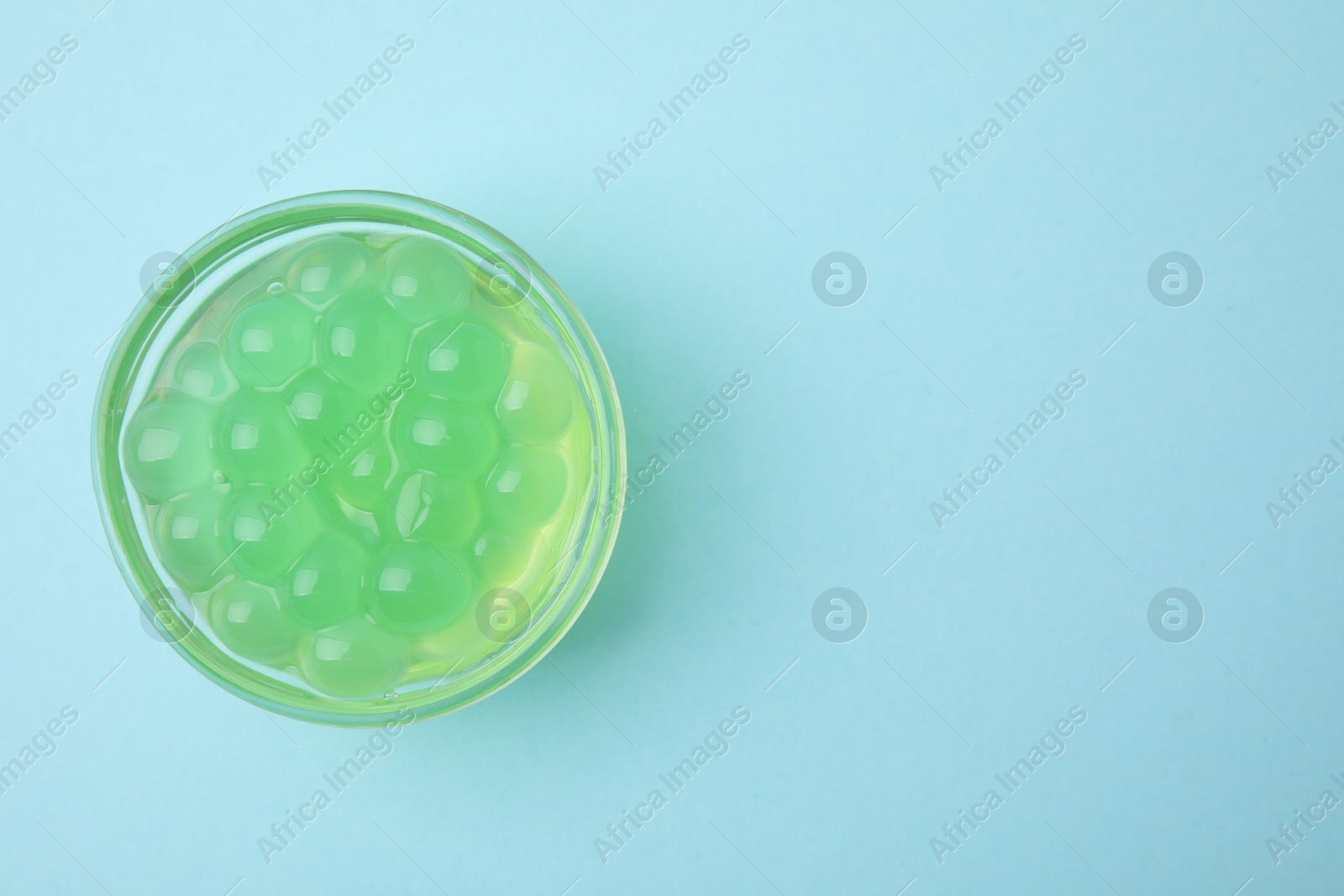 Photo of Bright tapioca pearls in bowl on light blue background, top view. Space for text