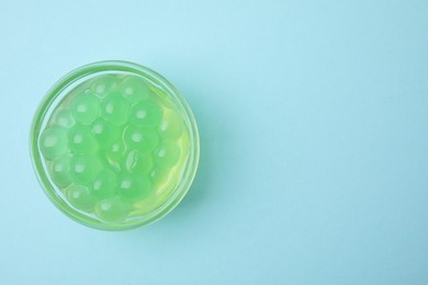 Photo of Bright tapioca pearls in bowl on light blue background, top view. Space for text