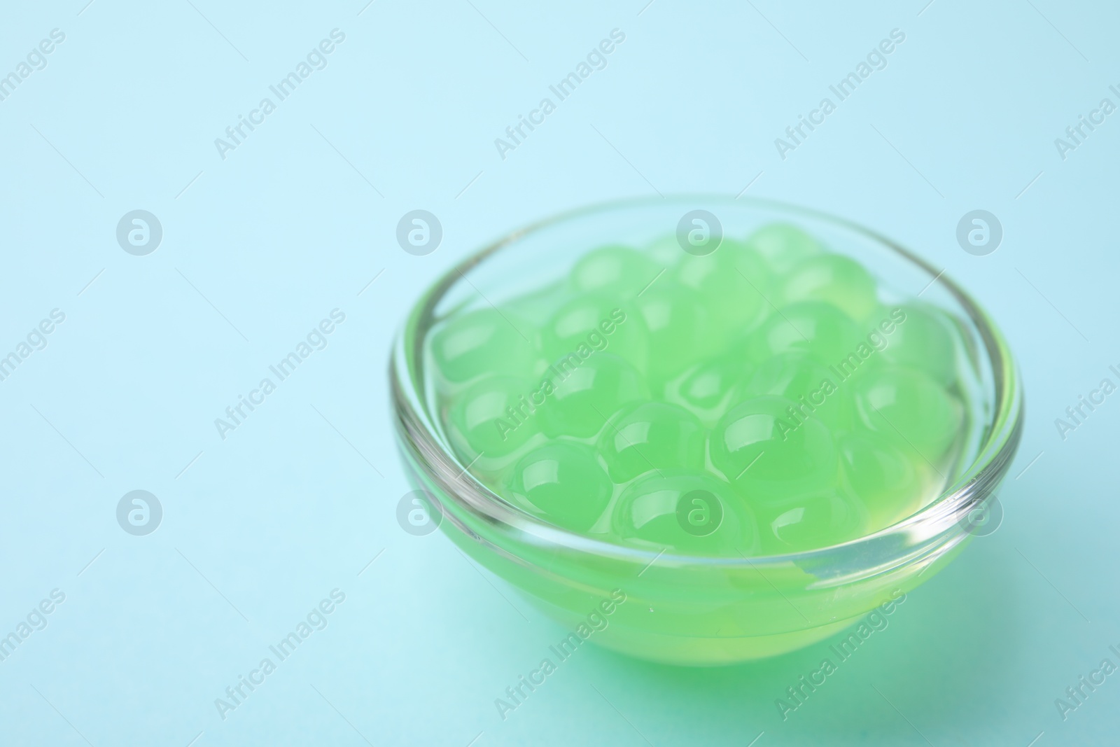 Photo of Bright tapioca pearls in bowl on light blue background, closeup