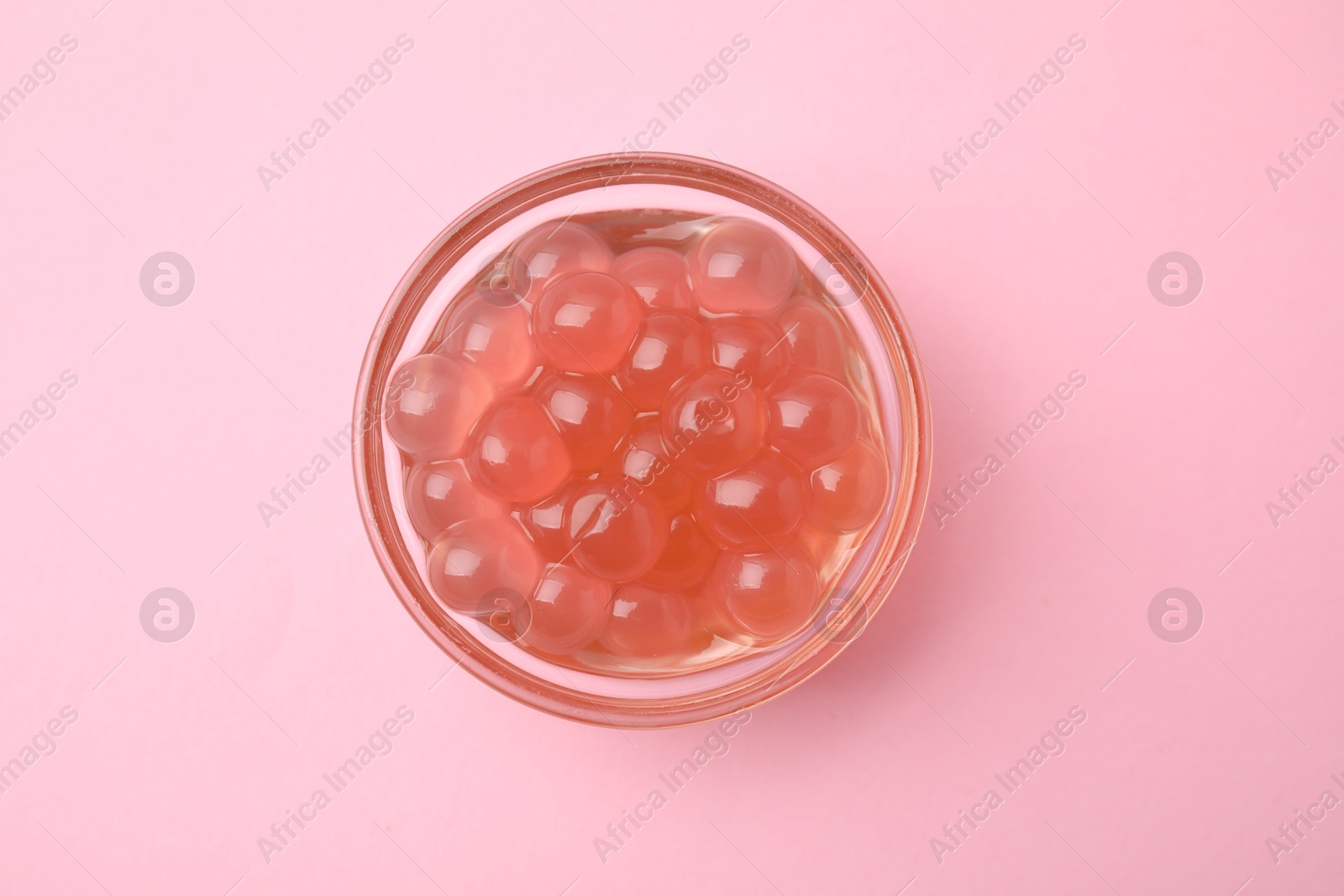 Photo of Bright tapioca pearls in bowl on pink background, top view