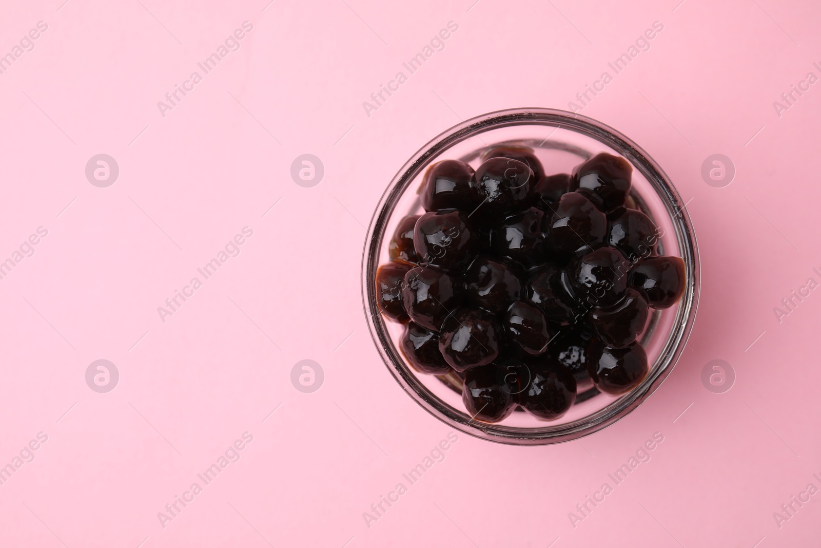 Photo of Dark tapioca pearls in bowl on pink background, top view. Space for text