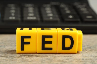 Photo of Cubes with letters Fed (Federal Reserve System) and calculator on wooden table, closeup