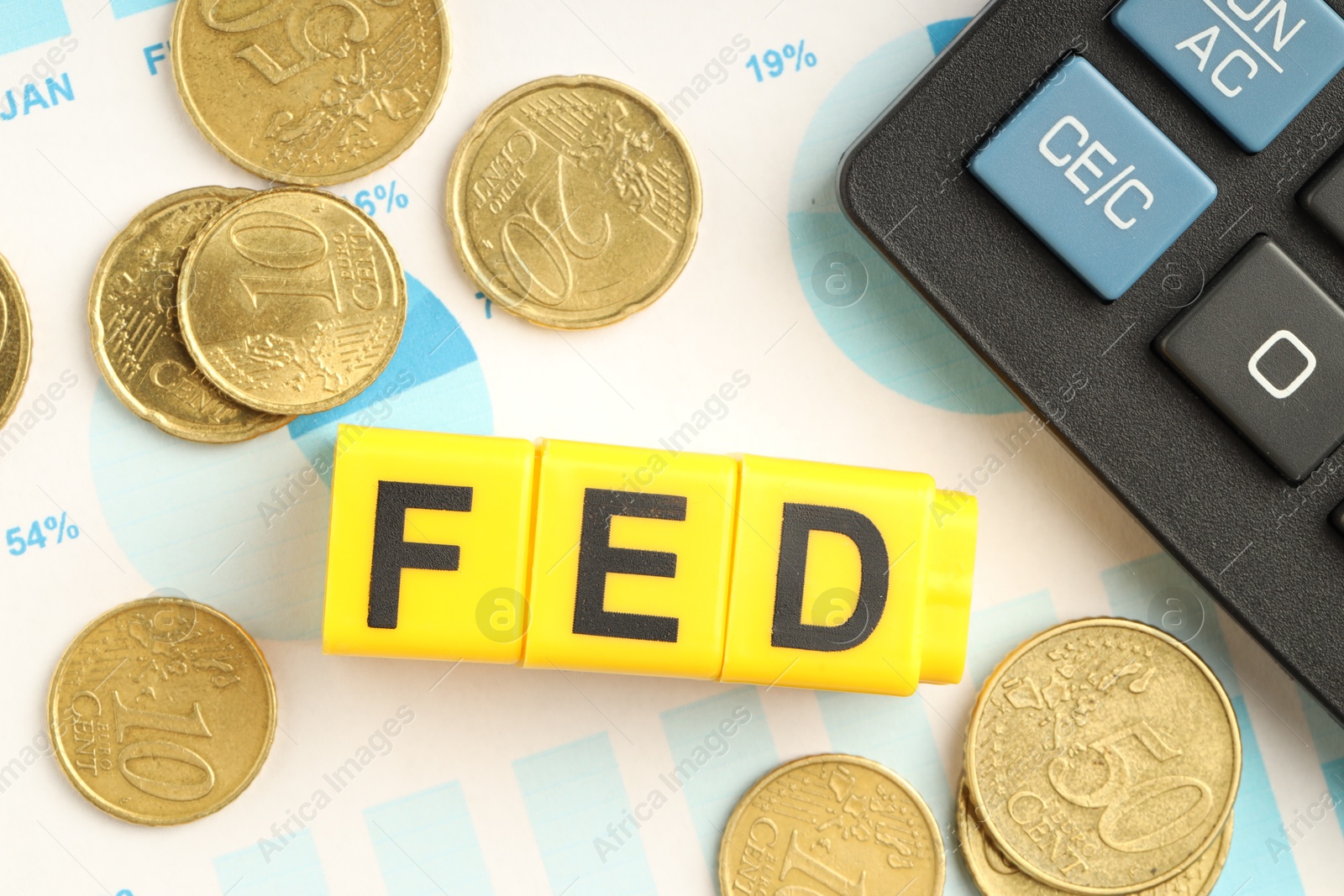 Photo of Cubes with letters Fed (Federal Reserve System), coins, calculator and paper with graphs, flat lay