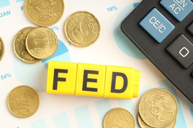 Photo of Cubes with letters Fed (Federal Reserve System), coins, calculator and paper with graphs, flat lay