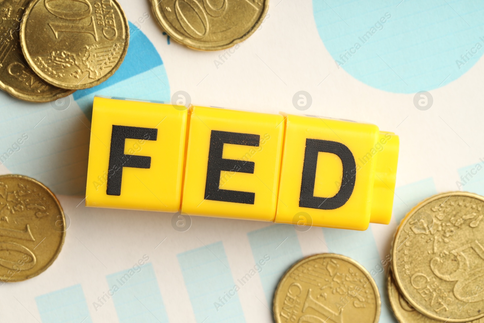 Photo of Cubes with letters Fed (Federal Reserve System), coins and paper with graphs, flat lay