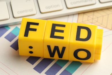 Photo of Cubes with letters Fed (Federal Reserve System) and paper with graphs, closeup