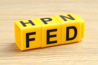 Photo of Cubes with letters Fed (Federal Reserve System) on wooden table, closeup