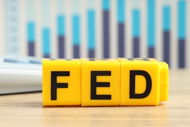 Photo of Cubes with letters Fed (Federal Reserve System) on wooden table, closeup