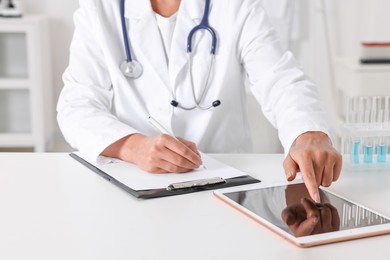 Doctor with tablet at table in clinic, closeup view