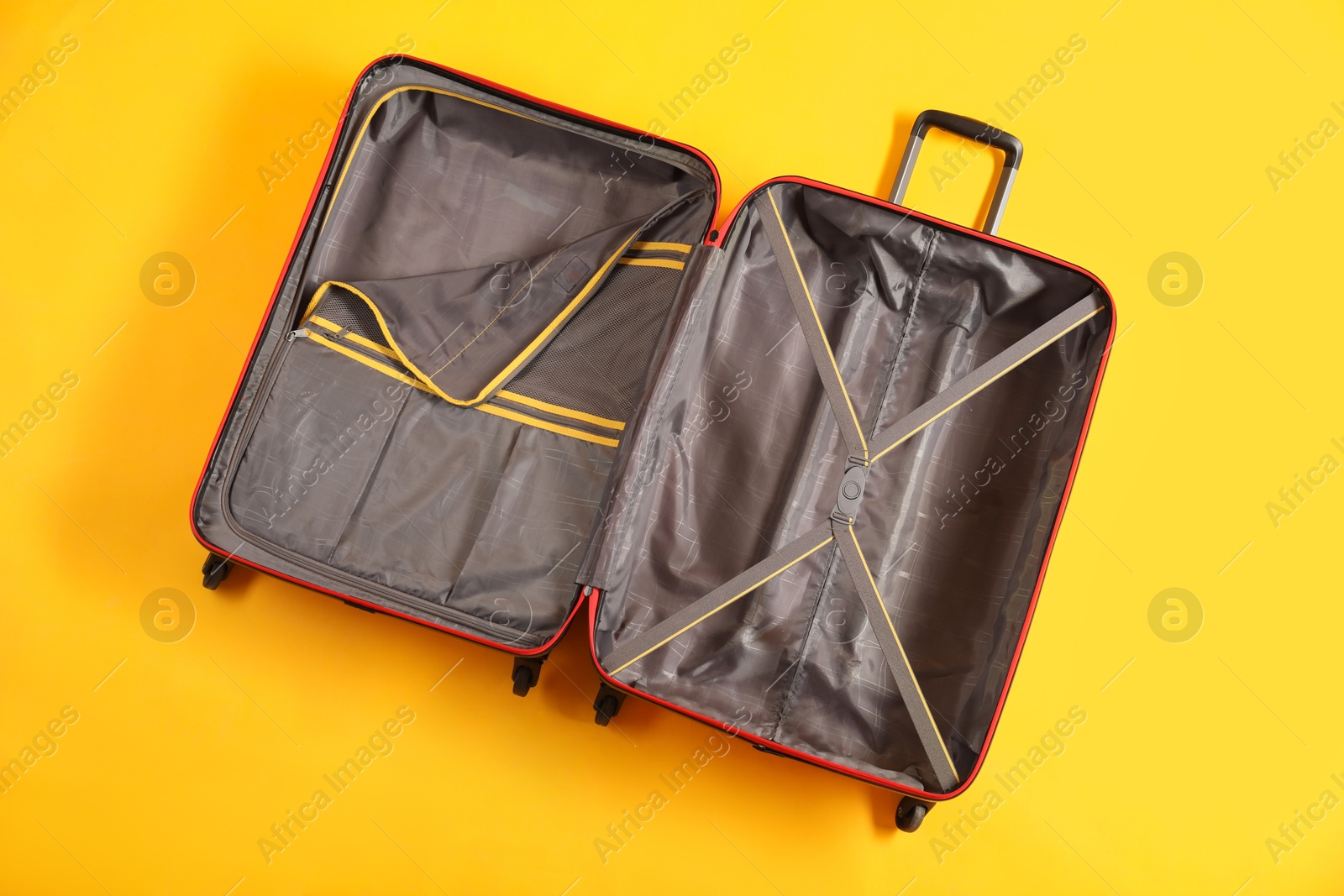 Photo of Open empty suitcase for travelling on yellow background, top view