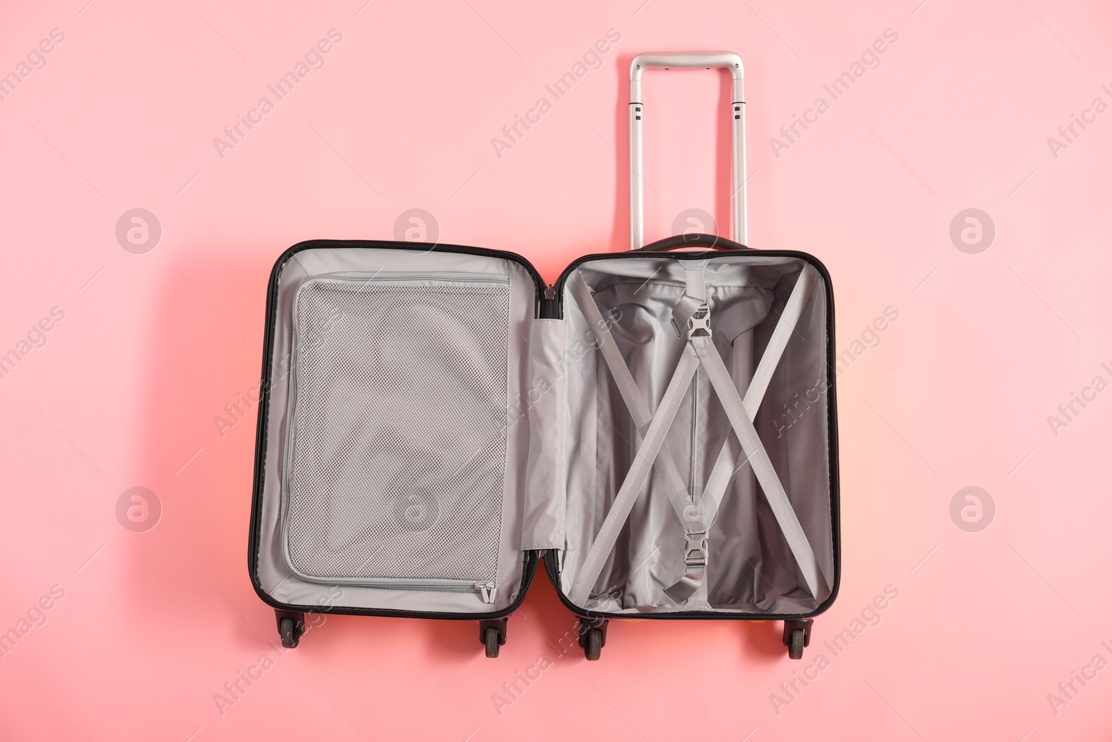 Photo of Open empty suitcase for travelling on pink background, top view